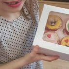 Close up of assorted decorated cupcakes in white box held by child