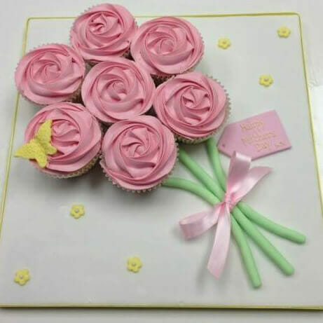 7 pink rose cupcakes on white board in bouquet arrangement and the words "Happy Mothers Day"