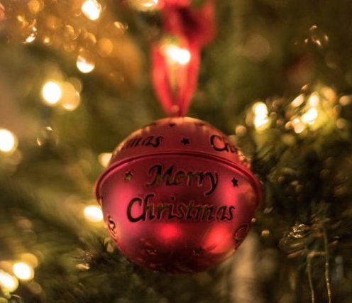 Close up shot of a traditional small red metal bauble on a lit Christmas tree