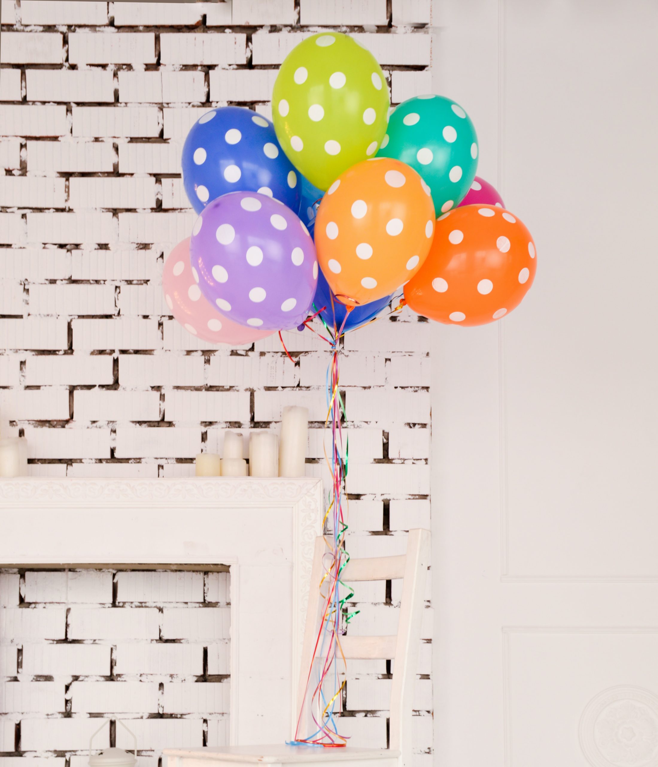 Multicoloured bunch of white spotted balloons tied to a chair on a white brick background