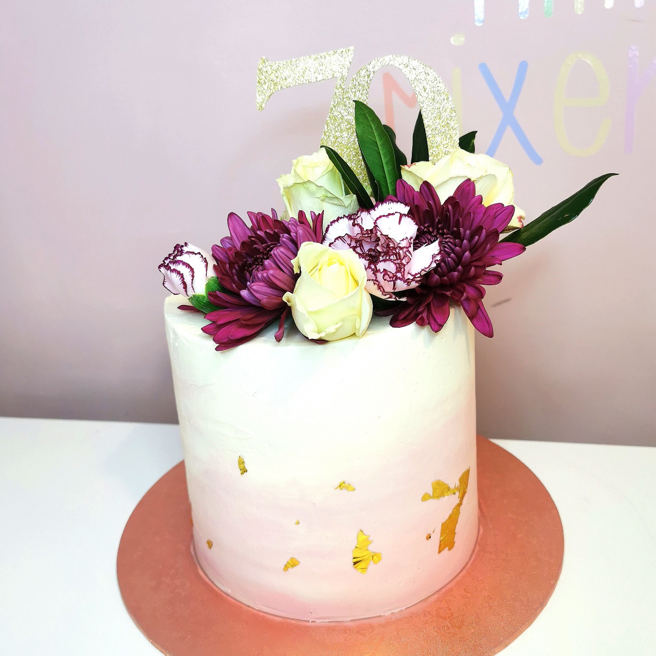 Tall pink and cream buttercream 70th birthday cake decorated with purple and cream flowers