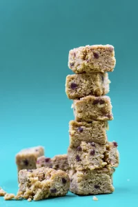 Pile of six cranberry flapjack cubes with 3 more cubes scattered on turquoise background