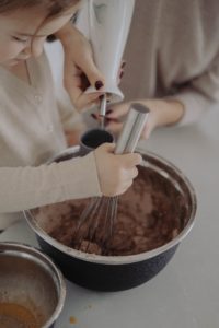 mother helping daughter stir chocolate cake mixture in kitchen