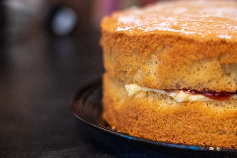 Vegan Victoria Sponge Cake dusted with icing sugar with jam and cream on black plate on a table