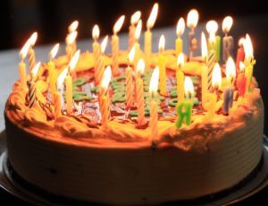 classic birthday cake covered in bright colours and lighted candles